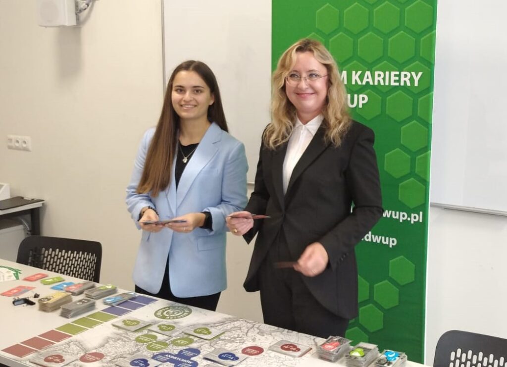 ZUS Kadra Centrum Kariery Przed Rozpoczęciem Rozgrywki Chłopskiej Szkoły Biznesu, Stoi Przy Stole Z Planszą Gry.