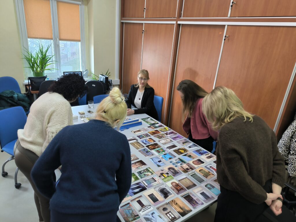 Grupa Kobiet Pochylona Nad Stołem, Na Którym Znajdują Się Karty Przedstawiające Fotografie Drzwi
